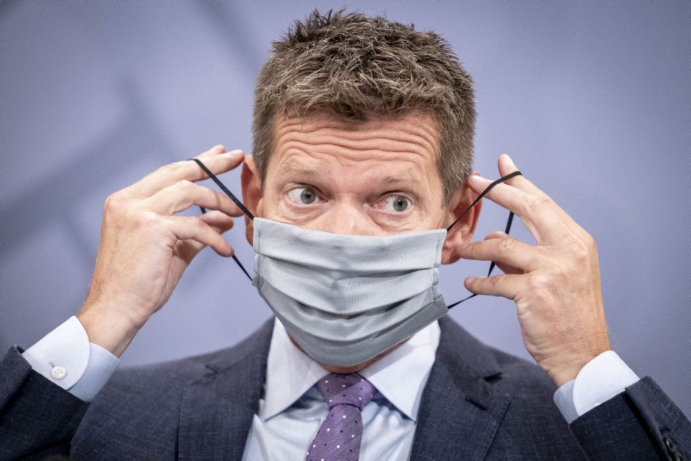 Sundhedsstyrelsens direktør Søren Brostrøm demonstrerer, under et pressemøde lørdag, hvordan et mundbind skal bruges korrekt. På billedet viser han et stofmundbind.