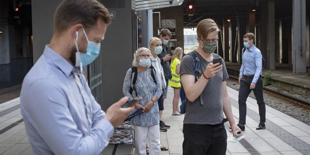 Mandag morgen har mange båret mundbind i den offentlige trafik i Aarhus. I baggrunden ses en person i en gul vest, der deler gratis mundbind ud. - 
