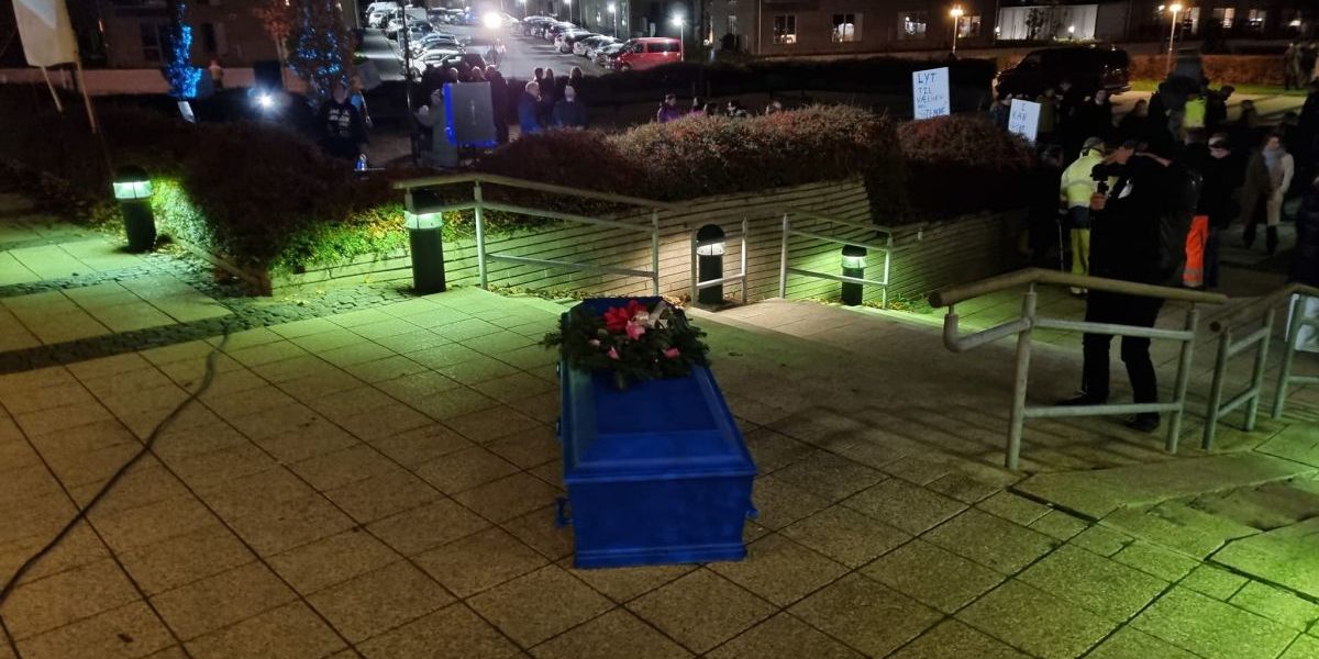 En blå kiste til at 'begrave Venstres politik i' blev båret frem af fire kistebærere og sat foran rådhuset i Helsinge ved demonstrationen mandag.
